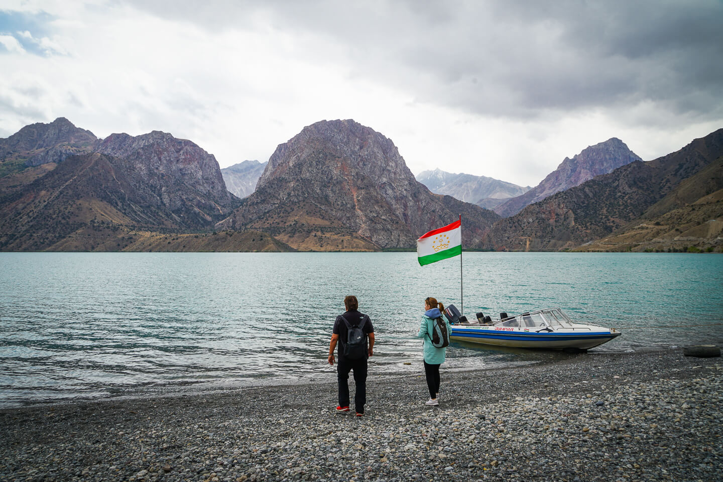 Iskanderkul lake shore with 2 travelers near the boat