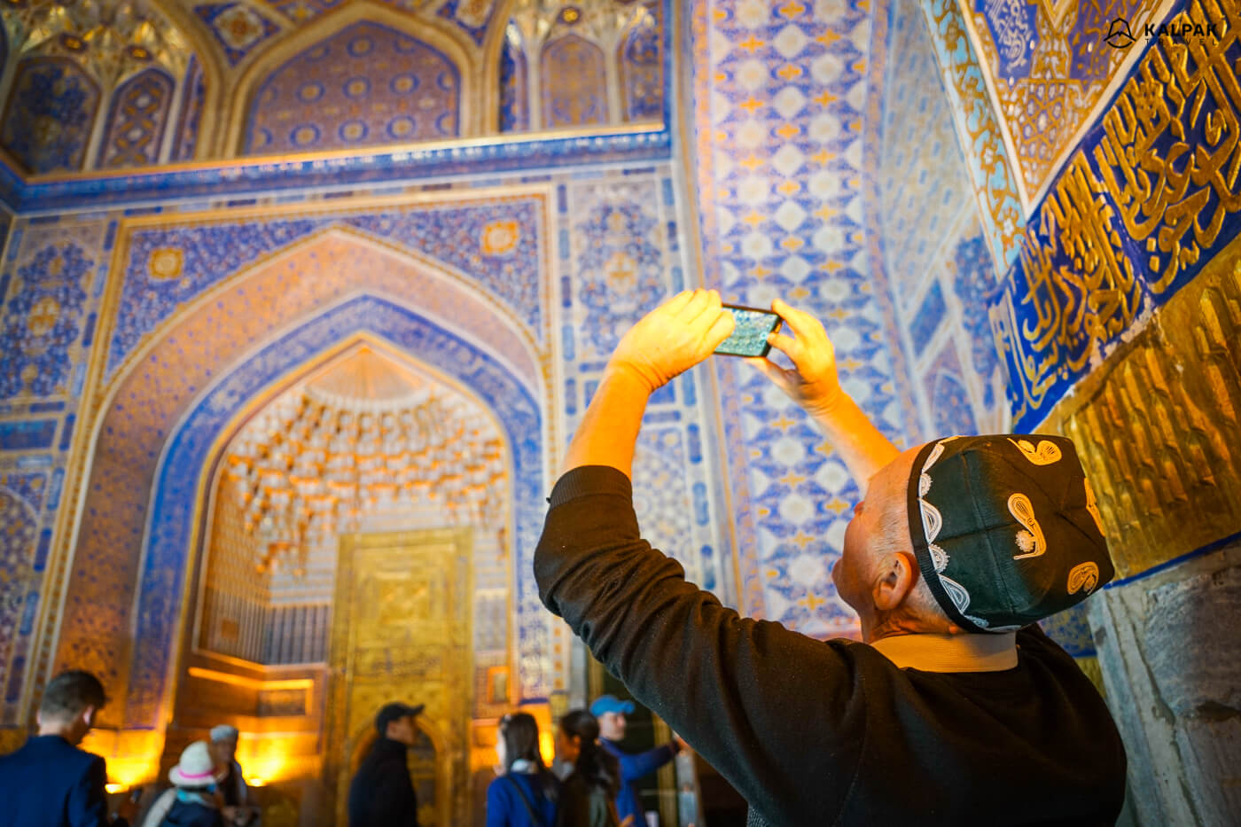 Golden building of Registan, men taking picture in national Uzbek hat